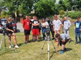 Grupa uczniów klasy VIII i licealistów stojąca na trawniku. Przed grupą stroją dwa teleskopy, w tle drzewa.
