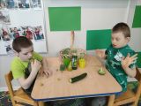 Dwóch uczniów szkoły podstawowej ubranych na zielono dotyka zielone warzywa i owoce