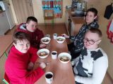 Czworo uczniów szkoły podstawowej przy stole. Na stole białe miski z makaronem i sosem pomidorowym