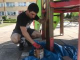 Gimnazjalista w ochronnych rękawicach impregnuje drewniany domek na szkolnym placu zabaw