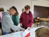 Dwóch chłopców wrzuca do urny wyborczej karty do głosowania. Za nimi grupa uczniów