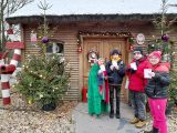 Troje uczniów z Elfem stoi przed chatą poczty Mikołaja. Uczniowie w ręcach trzymają listy.