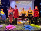 Pięć dziewczynek w przebraniach owadów stoi na scenie trzymając się za ręce. Przed nimi na podłodze leżą kolorowe kwiaty