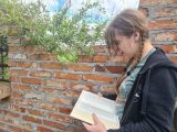 Nastolatka z warkoczykami czytająca książkę na tle ściany z cegieł.