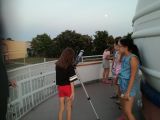 Na balkonie obserwatorium dziewczynka ze szkoły podstawowej obserwuje niebo przez teleskop. Przy okrągłej kopule stoją...