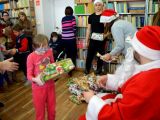 Uczennica szkoły podstawowej odbiera prezent od św. Mikołaja. W tle inne dzieci i dorośli.